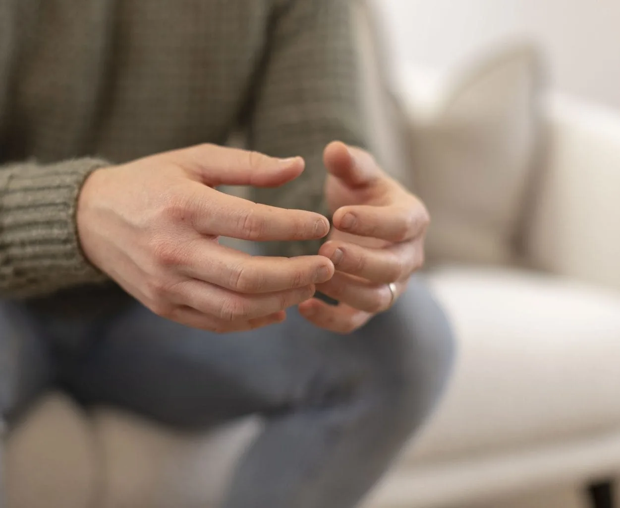 A person sitting in a therapy session, hands gently clasped together in a natural resting position
