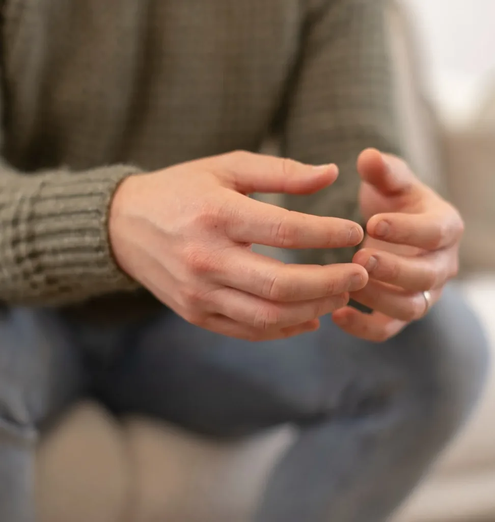 Close-up of a person's clasped hands as they sit and talk during a therapy session