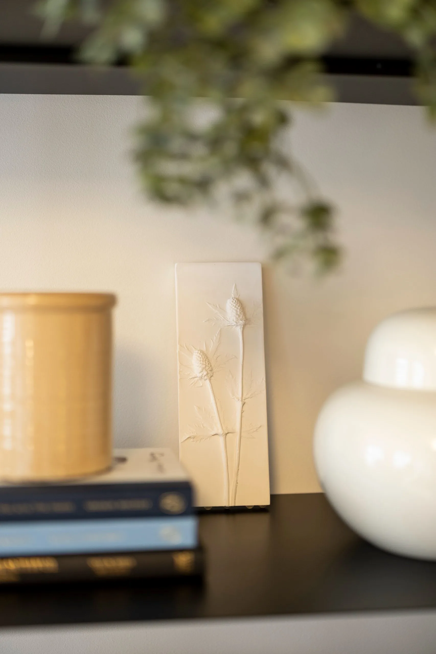 Close-up of a white botanical plaster cast of thistles on a black shelf beside ceramics and books at London Bridge Therapy