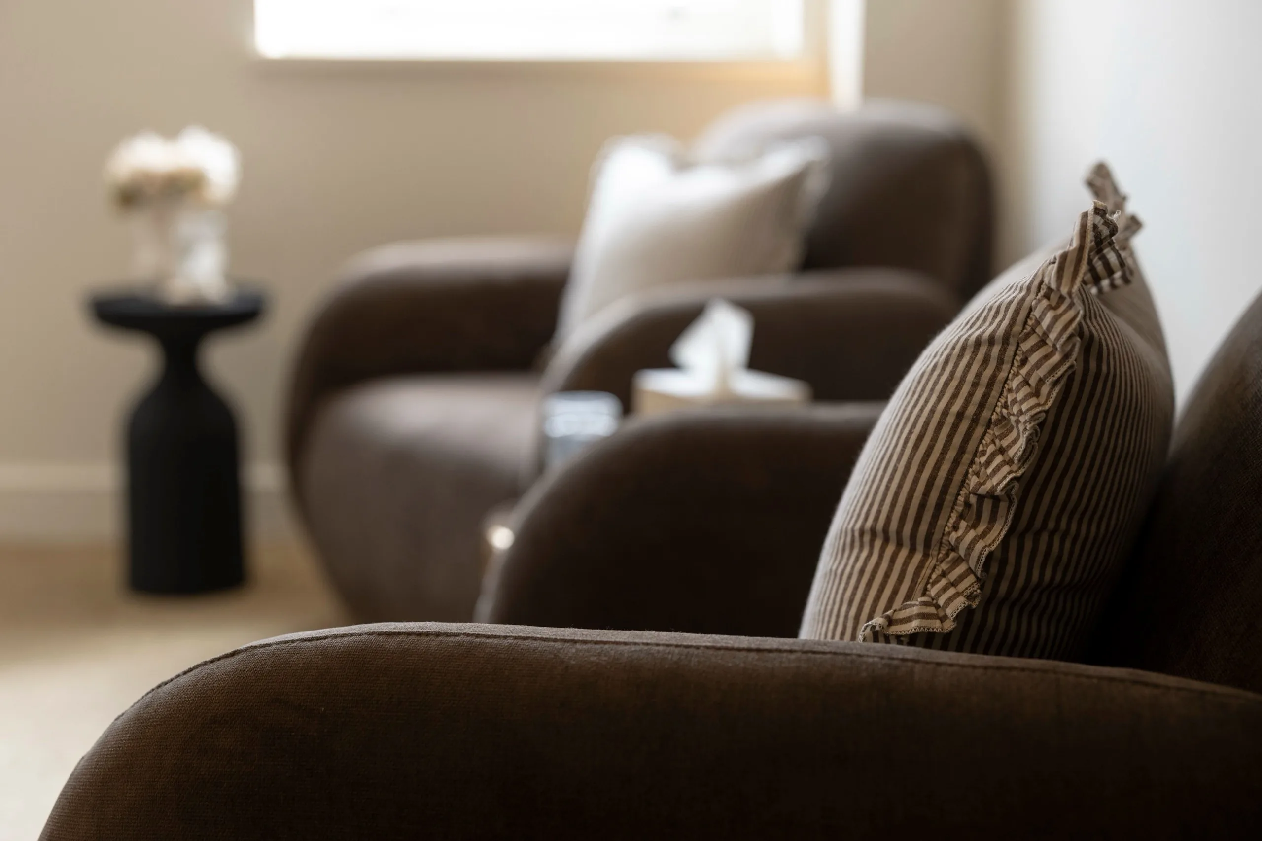 Two armchairs facing each other in a therapy room, with a side table and tissues between them